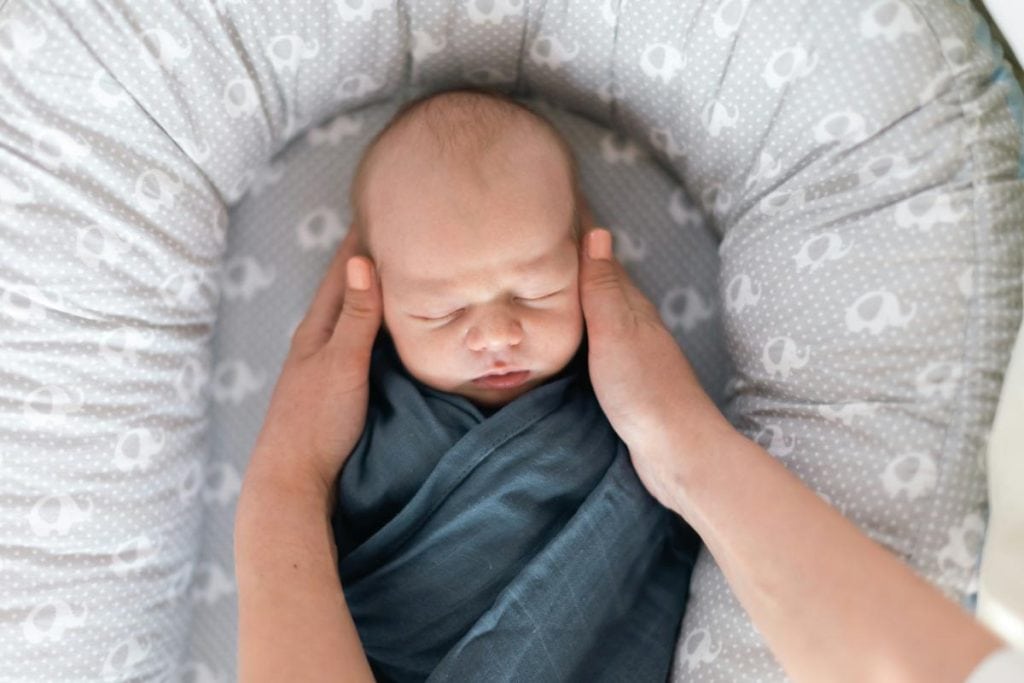 mother putting swaddled infant in bassinet