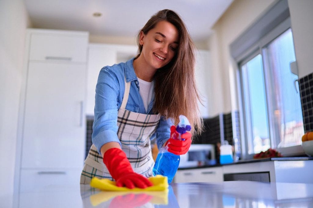 woman wearing an apron and cleaning gloves wiping down kitchen counters