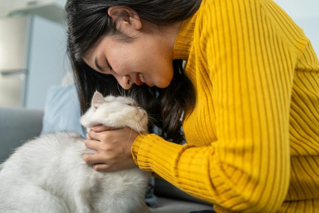 woman smiling at and petting her cat