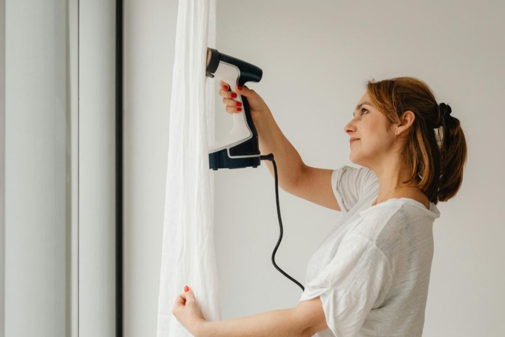 woman steaming curtains to get the wrinkles out