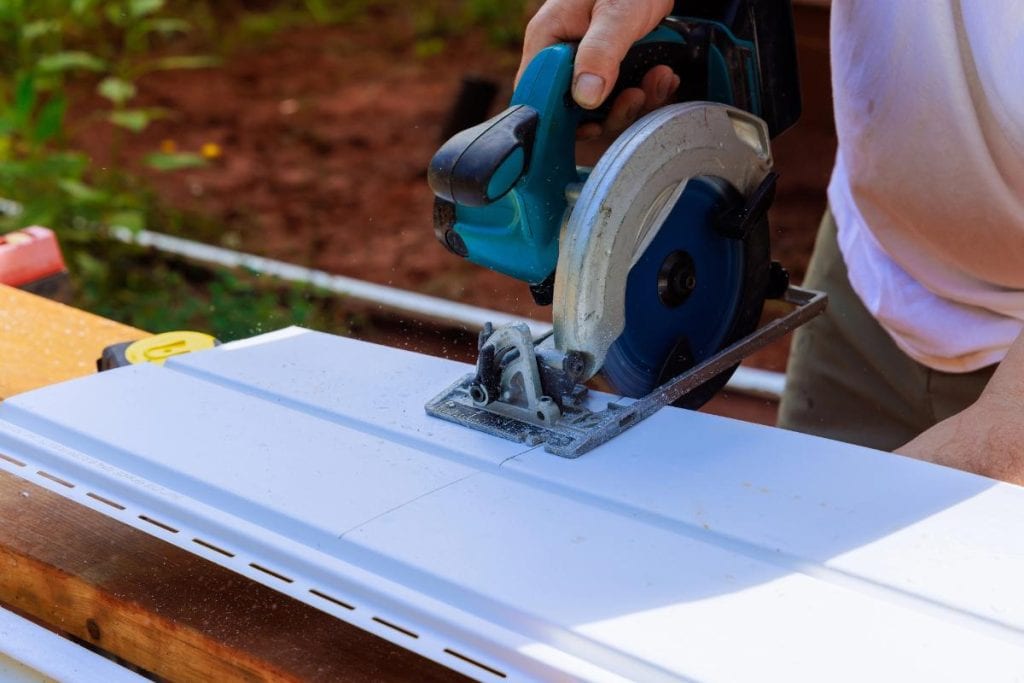 man using a saw to cut vinyl siding