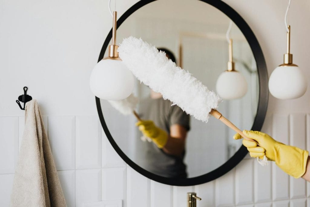 dusting a light fixture in front of a mirror