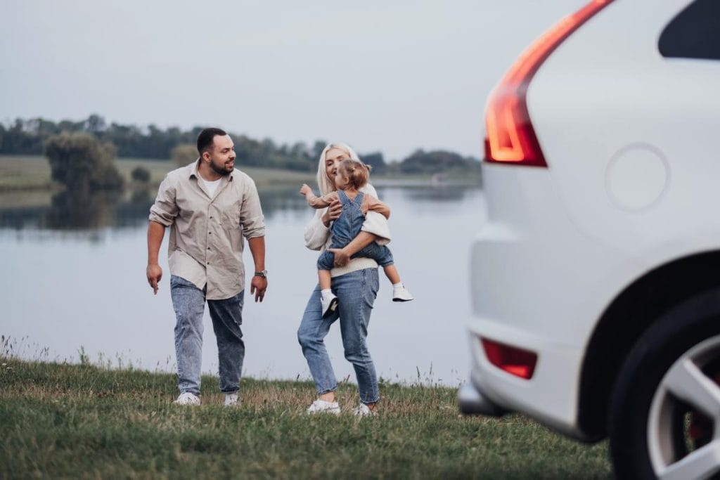 mom, dad, and toddler walking near a lake with SUV parked in foreground