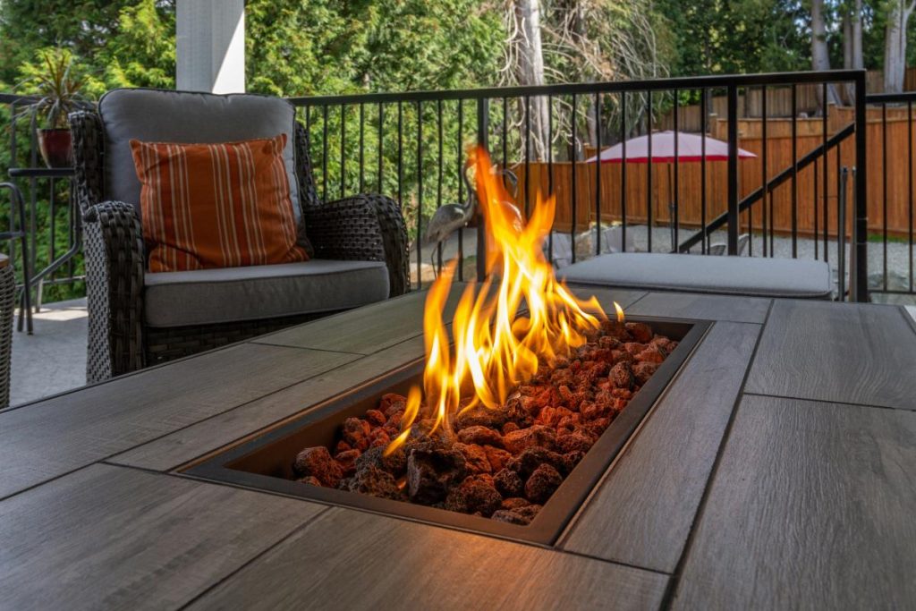 a fire pit table on a deck in the backyard