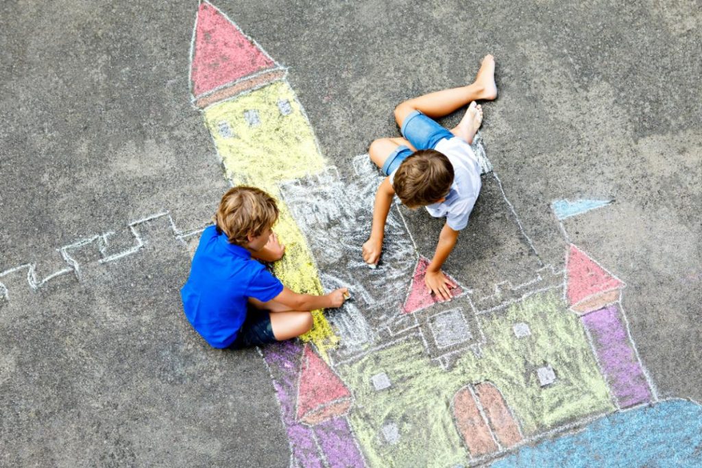 kids coloring in a chalk drawing of a castle on a driveway