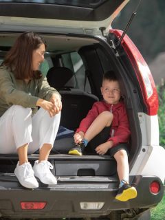 mom and son sitting in the open trunk of an suv while taking a break from driving