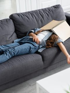 young woman laying on couch with notebook on face