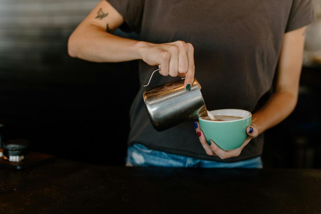 person pouring creamer into coffee