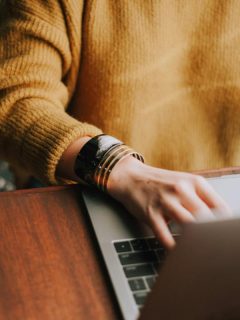 person in goldish orange sweater using a laptop