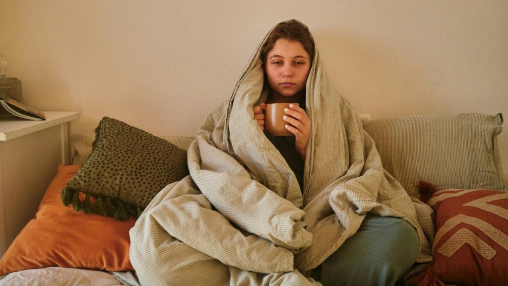 sick woman with coffee wrapped in blanket on couch