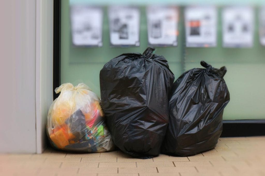 three trash bags lined up outside a store