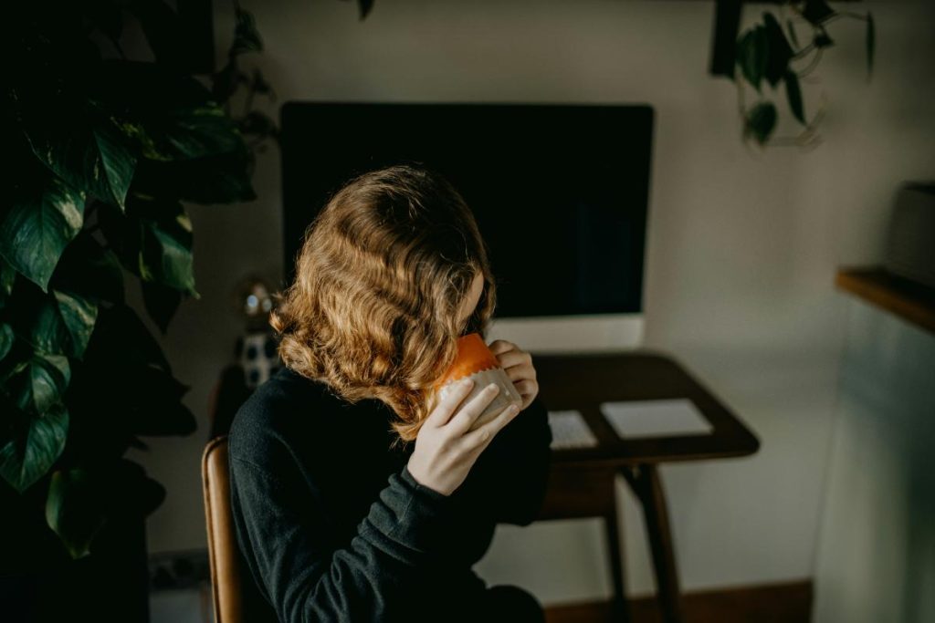 woman drinking coffee in front of desktop computer