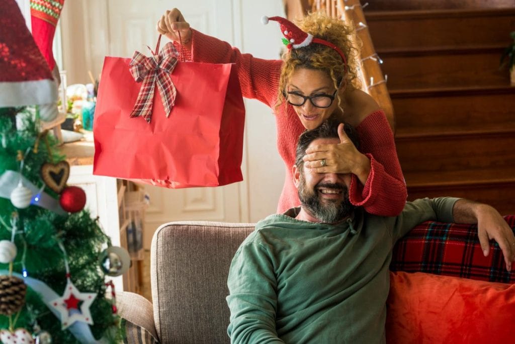 wife covering husband's eyes to give him a christmas gift