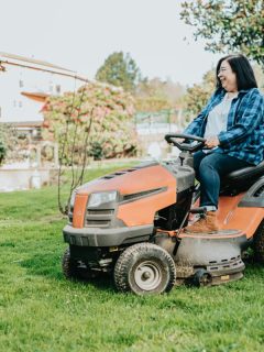 woman in flannel shirt in backyard on a riding mower