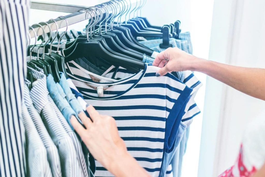 woman choosing a navy and white striped shirt from a rack of clothes