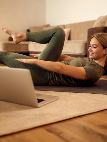 woman on rug in living room using a laptop to watch a video while exercising