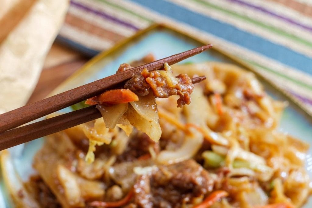 a pair of chopsticks holding up a bite of beef chow fun