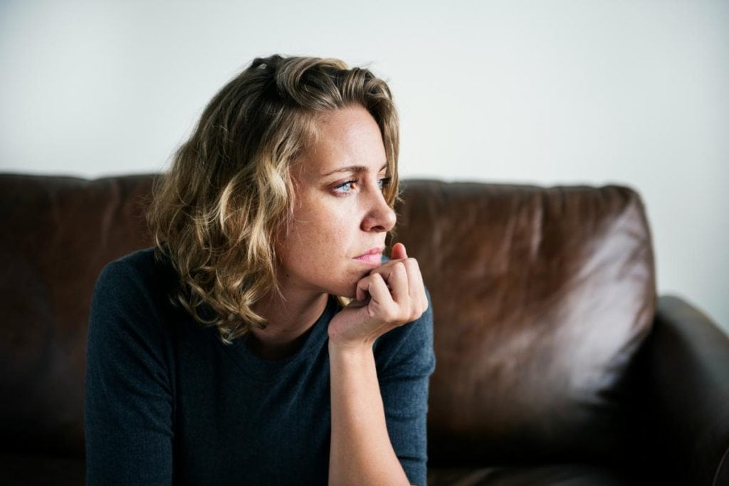 blonde woman sitting on leather couch looking away from the camera and thinking