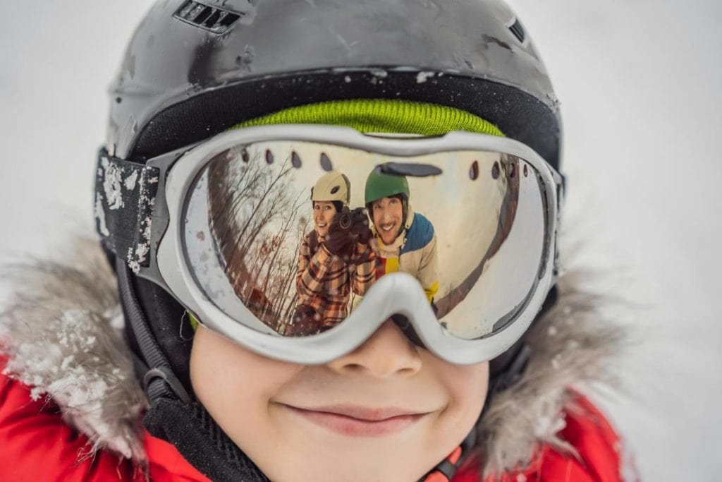 boy wearing ski goggles with parents reflected in the lenses