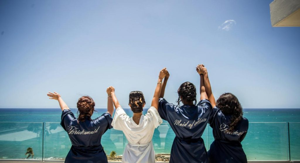 bride and bridesmaids holding hands and overlooking the ocean