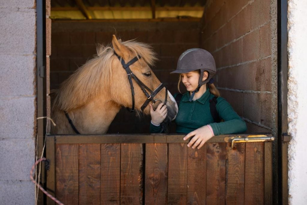 girl in riding helmet standing by a horse in a stable