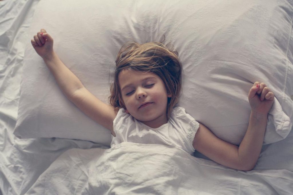 sleeping girl with arms spread wide on white pillow