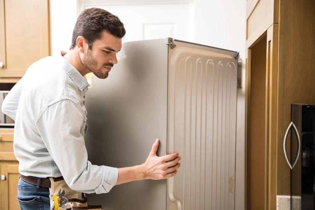 man moving a fridge to inspect it 