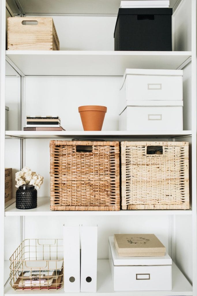 a home office with various storage boxes and baskets on bookshelf