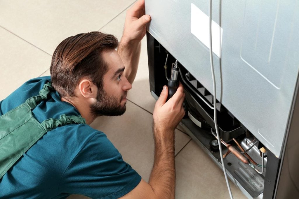 man using tools to repair fridge