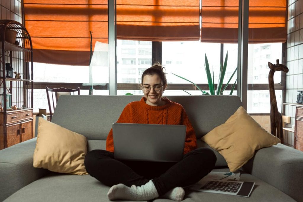 woman in orange sweater using a laptop computer for online learning