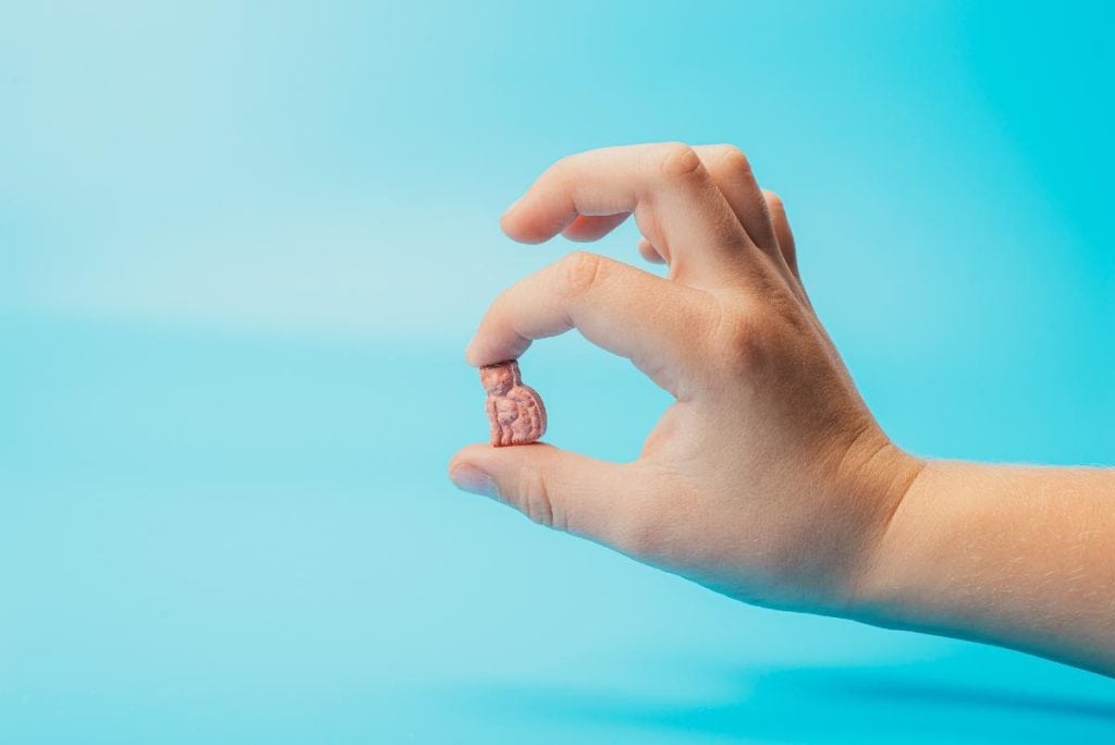 child's hand holding a vitamin between finger and thumb