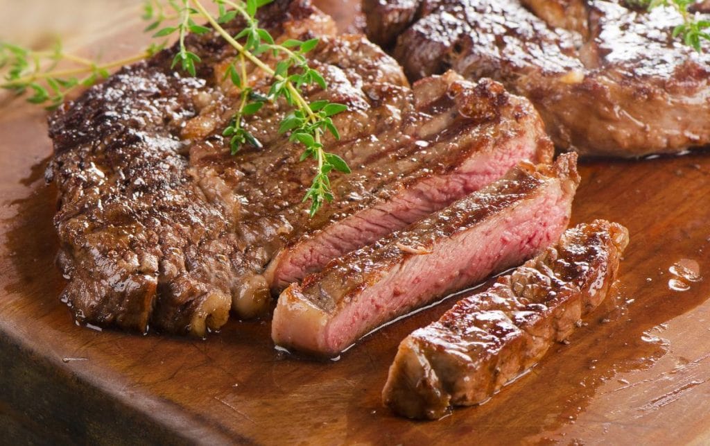 grilled and sliced ribeye steak on wooden cutting board