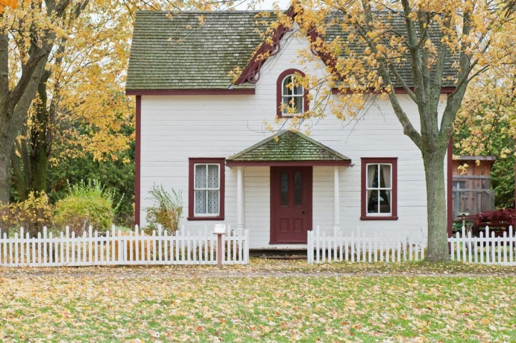 small white house with red trim and a fence in the autumn