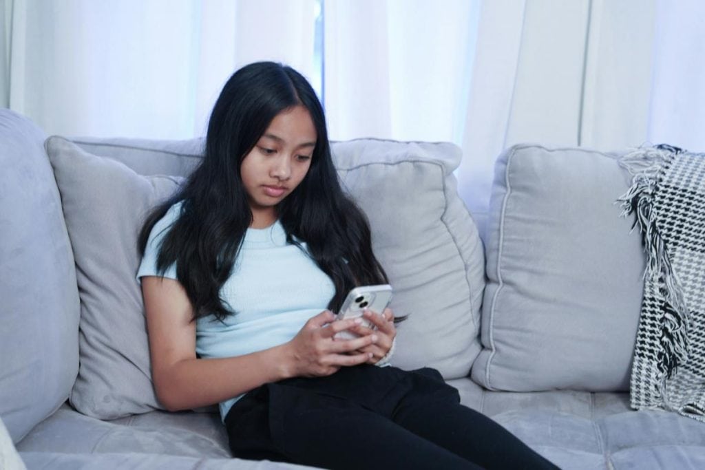 teen girl sitting on couch using smartphone