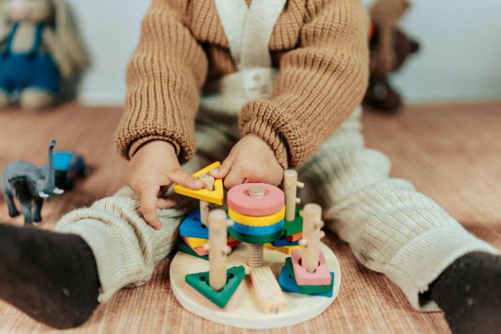 toddler girl sitting on floor playing with wooden toys