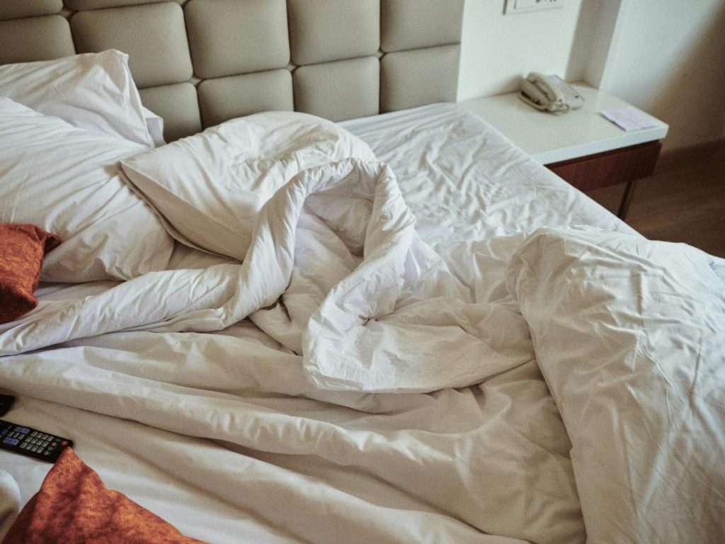 an unmade bed with white sheets and comforter