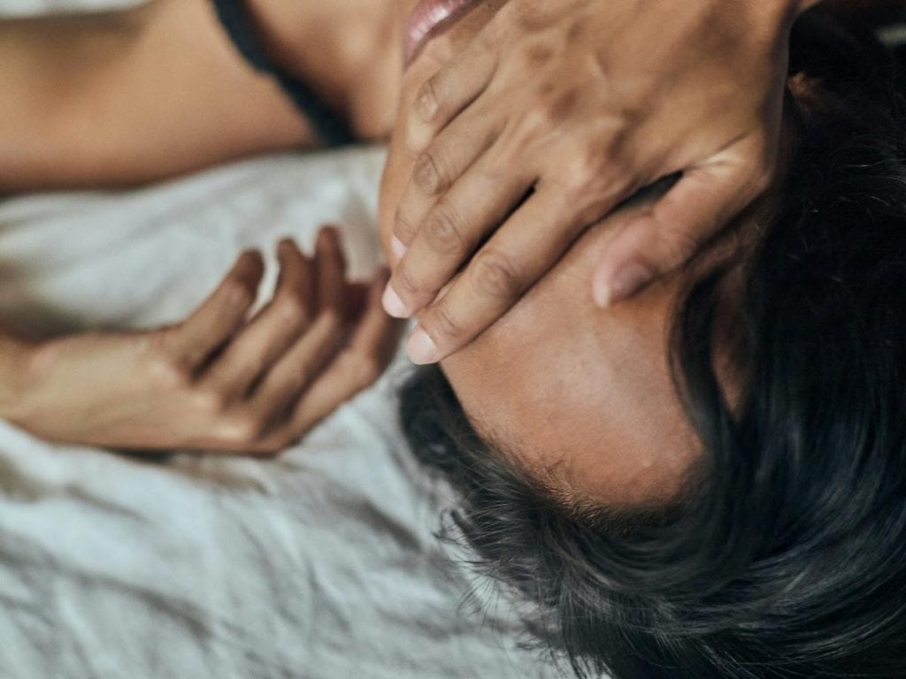 woman laying on bed covering face with hand