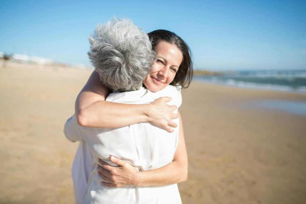 a woman hugging her elderly mother on the beach