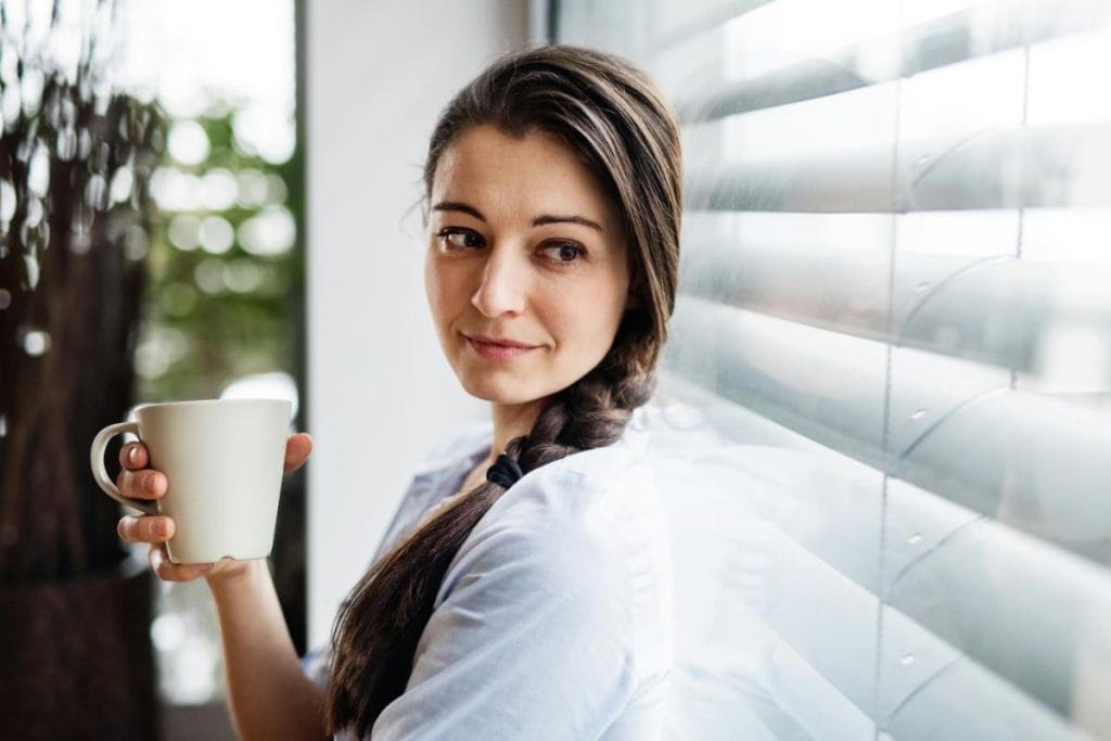 woman with braided hair drinking coffee near window