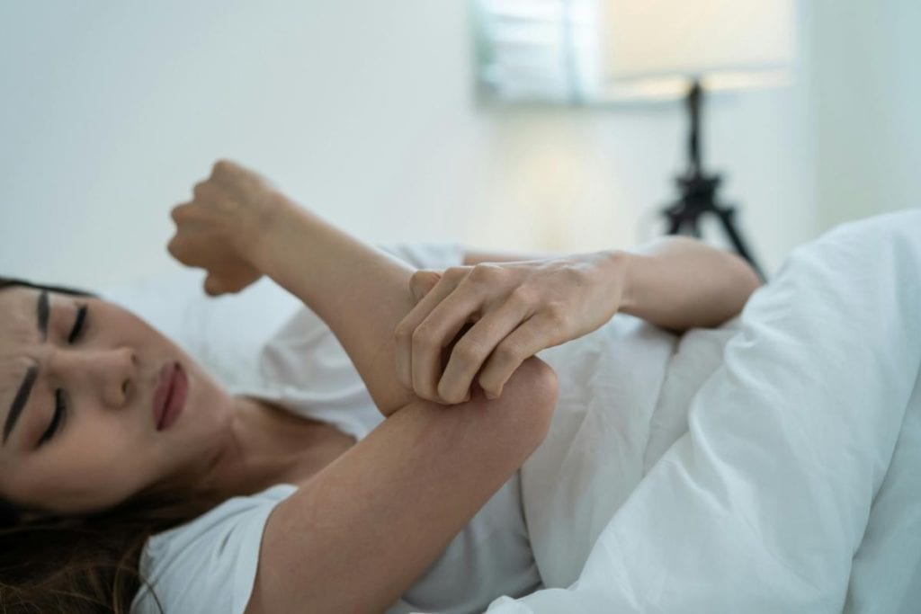 woman scratching her arm while laying in bed