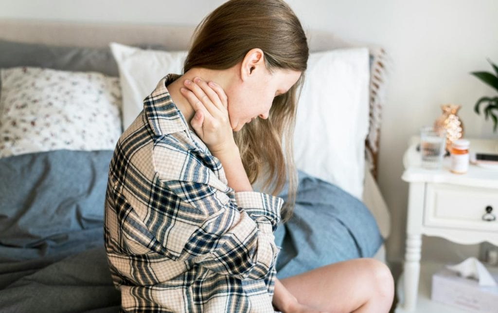 woman with neck pain sitting on edge of bed