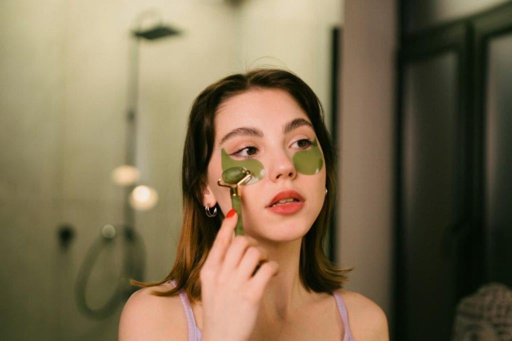 woman using facial roller and undereye masks