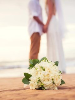 couple married on beach with white bouquet in focus