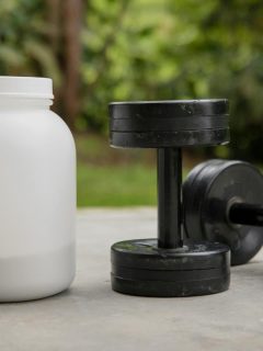 container of whey protein sitting beside dumbbells