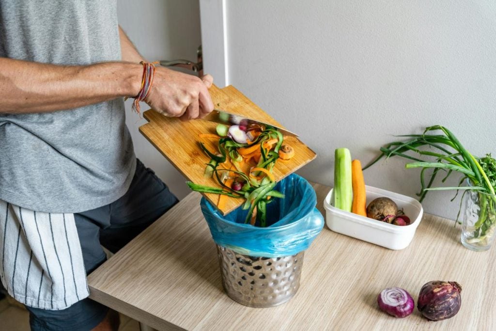 person putting food waste into a small bin