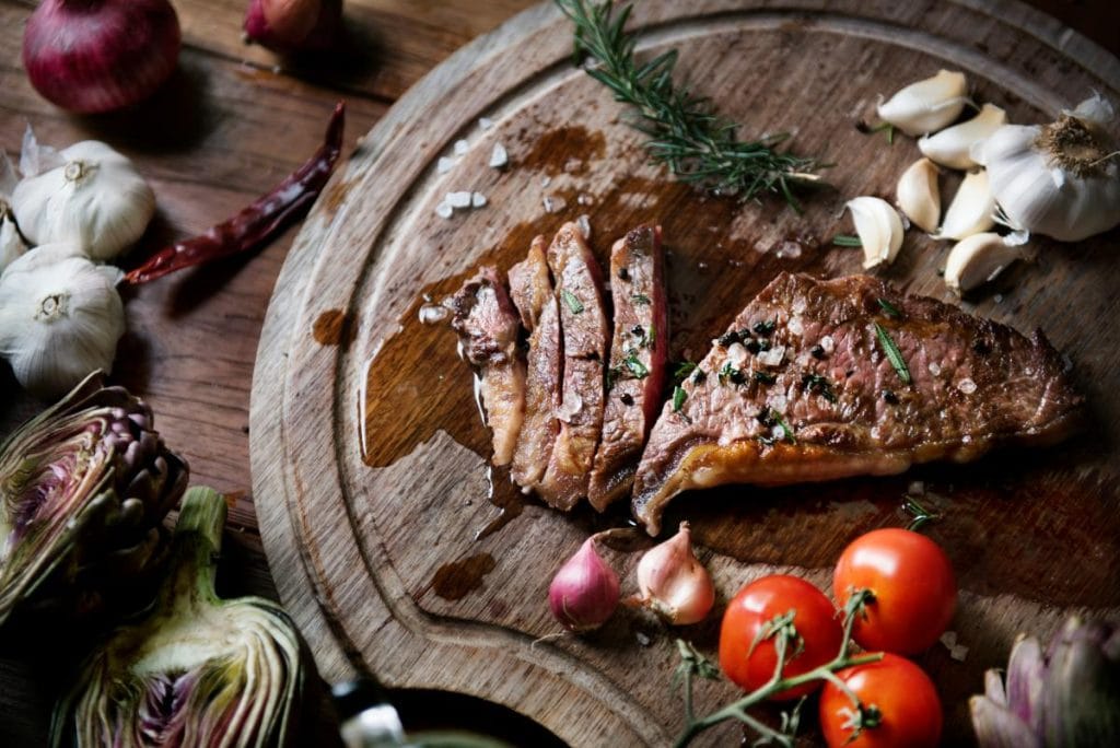 sliced steak on a wood cutting board with cherry tomatoes and garlic