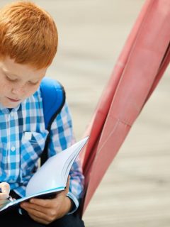 young red haired boy in plaid shirt writing in notebook while on a swing