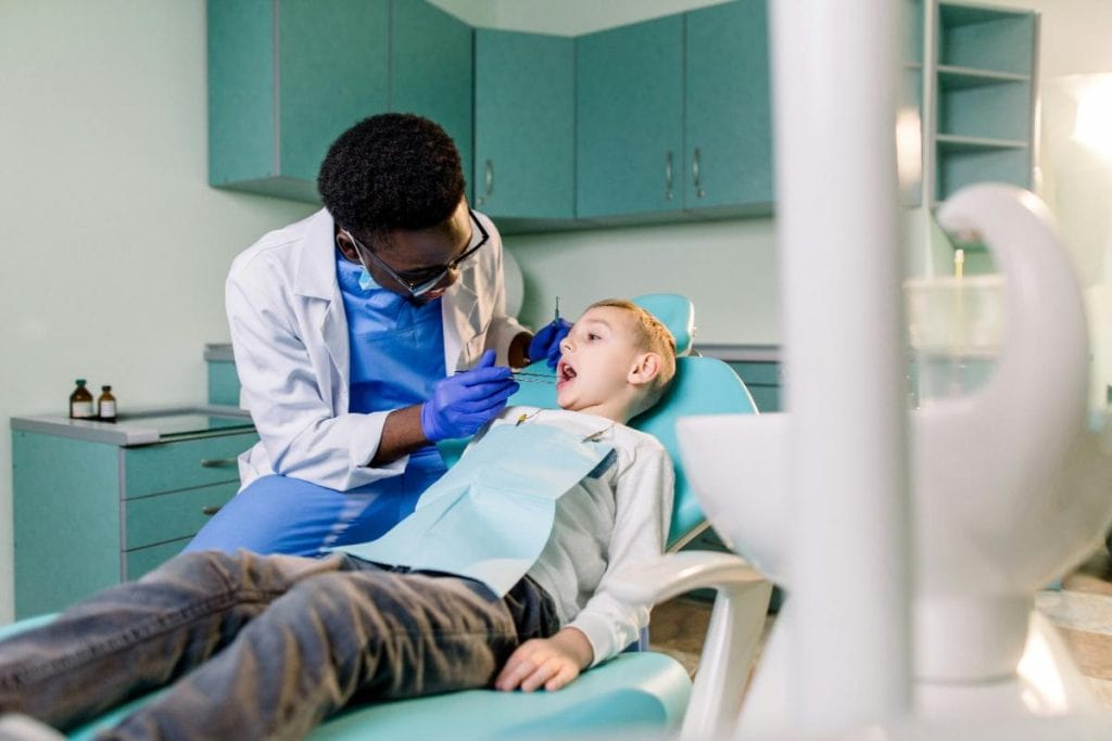 little boy in dentist's chair with dentist examining teeth