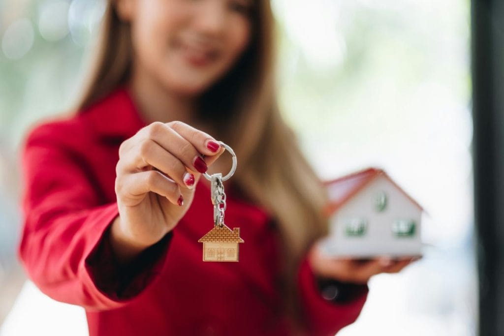 real estate agent in a red jacket holding a model home and keys