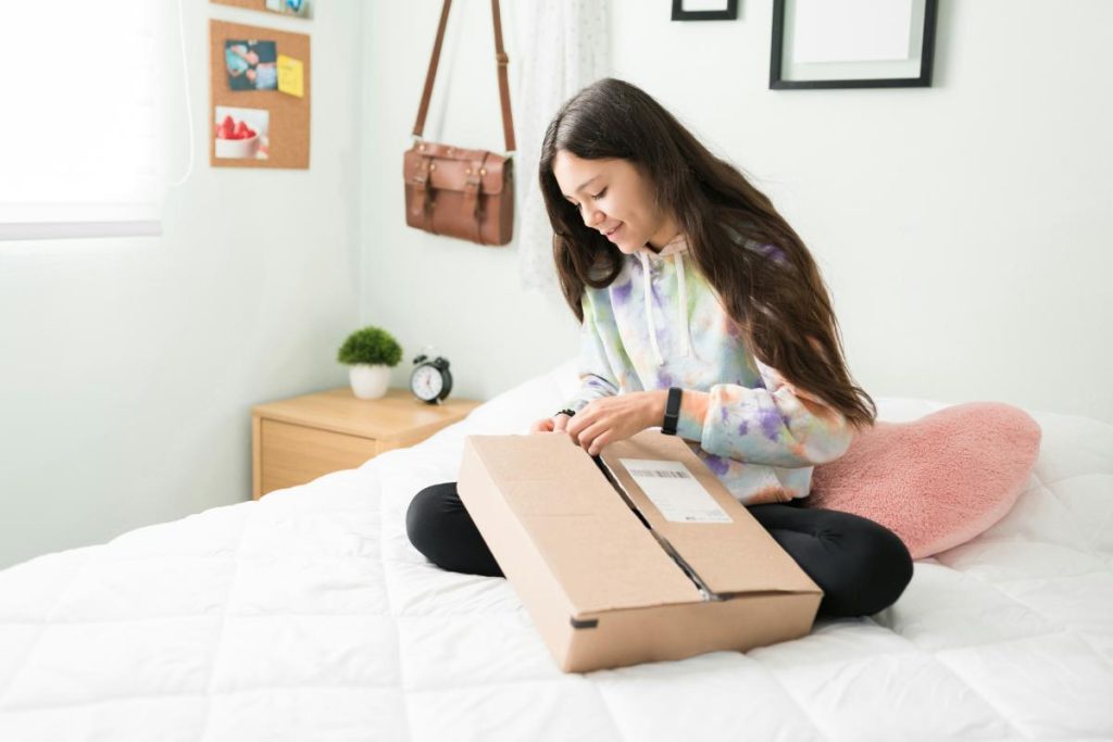 teenage girl sitting on bed opening a box